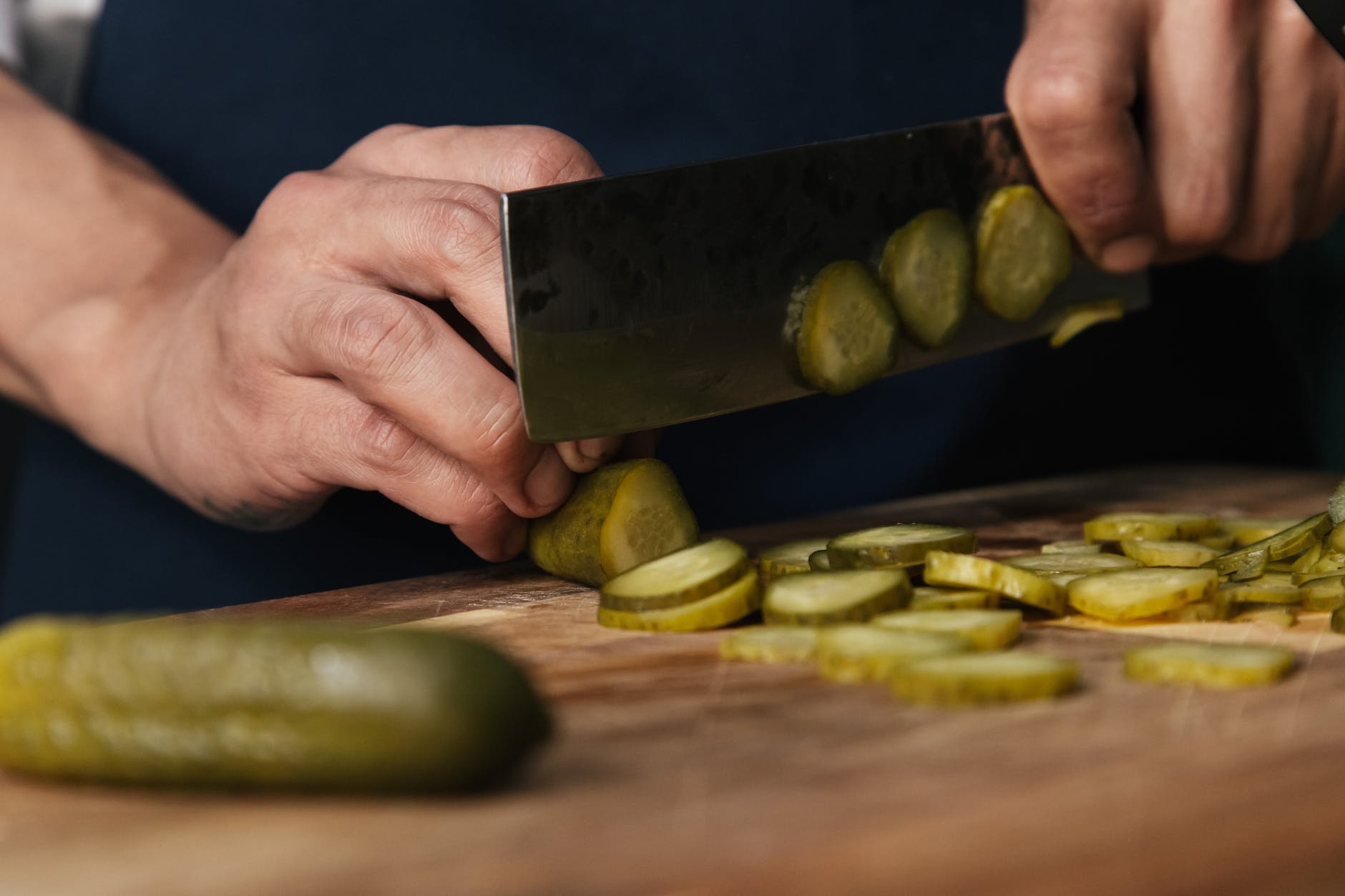 person slicing pickles on a wooden chopping board