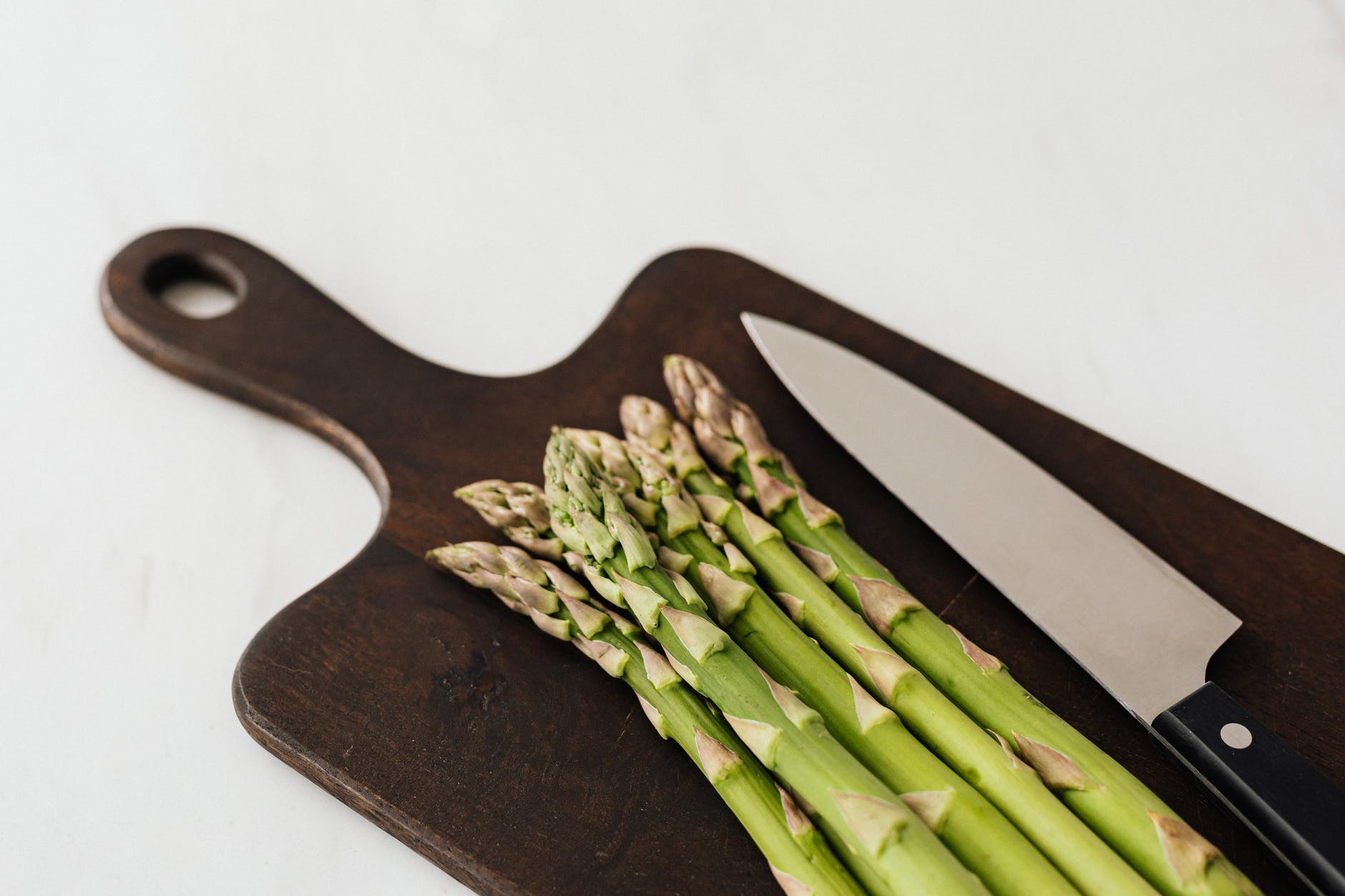 knife and asparagus on wooden board